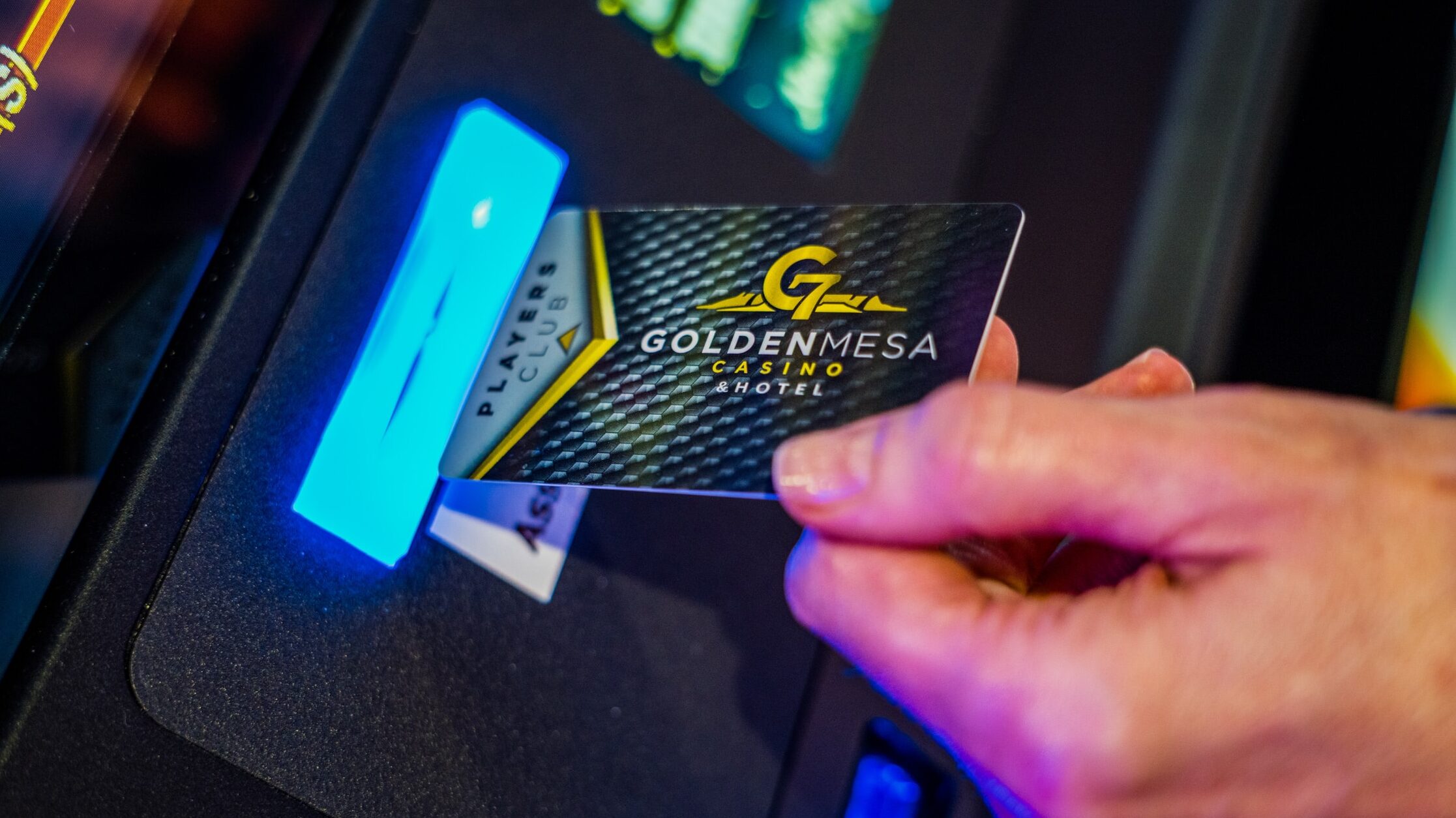 Close-up of a guest inserting a Golden Mesa Players Club card into an electronic game, with colorful casino lights glowing.