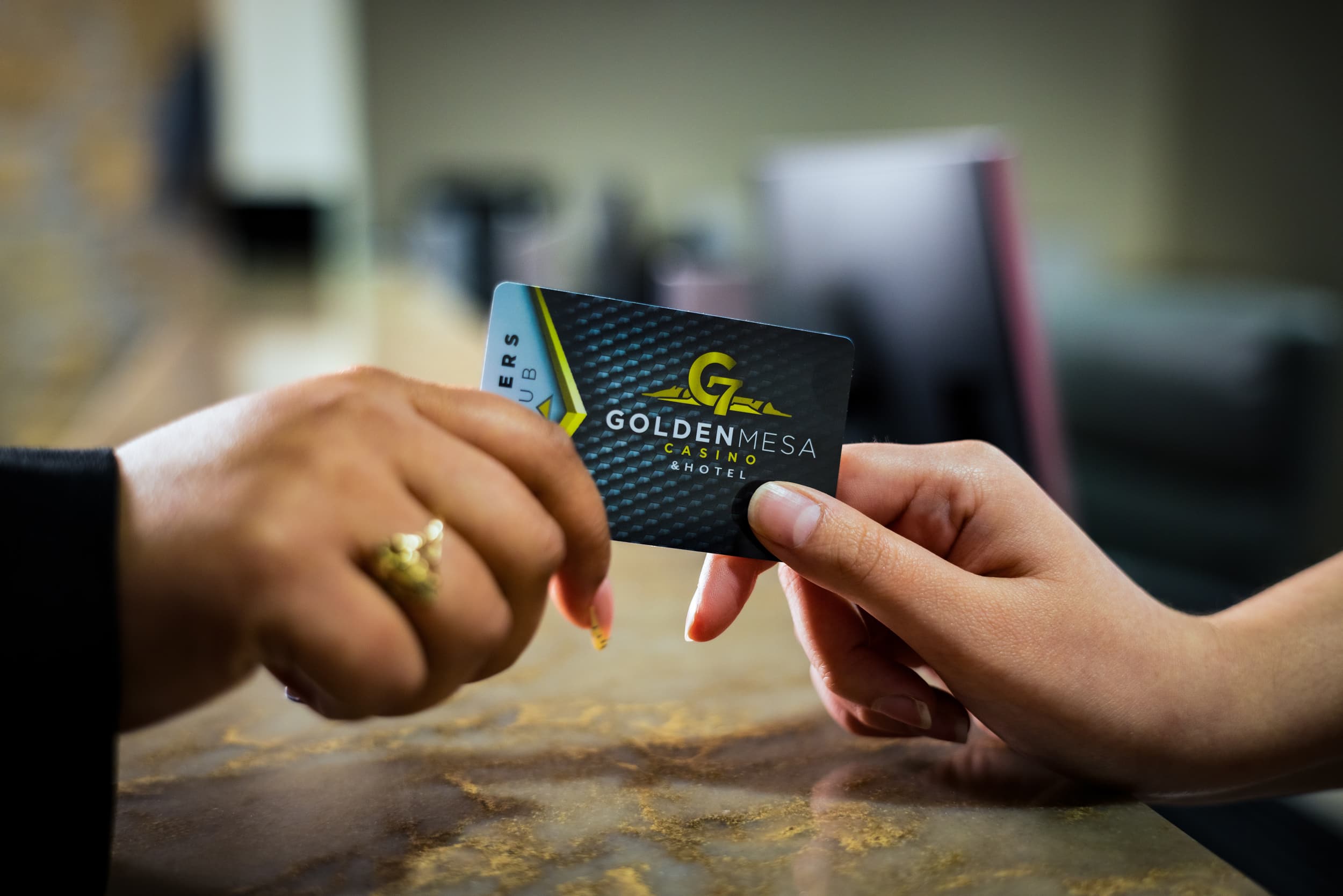 Close-up of the hands of a Golden Mesa Casino employee handing a Players Club card to a player at the Players Club desk.