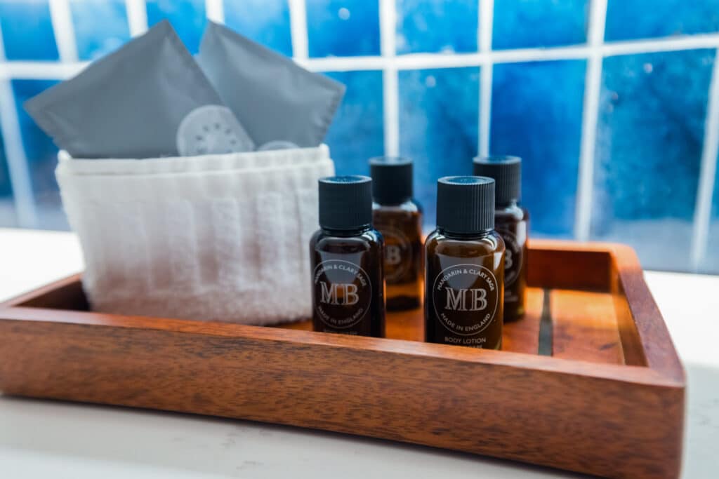 Bathroom amenities arranged on a wood tray with folded towels and blue tile behind them in a Golden Mesa Hotel room.
