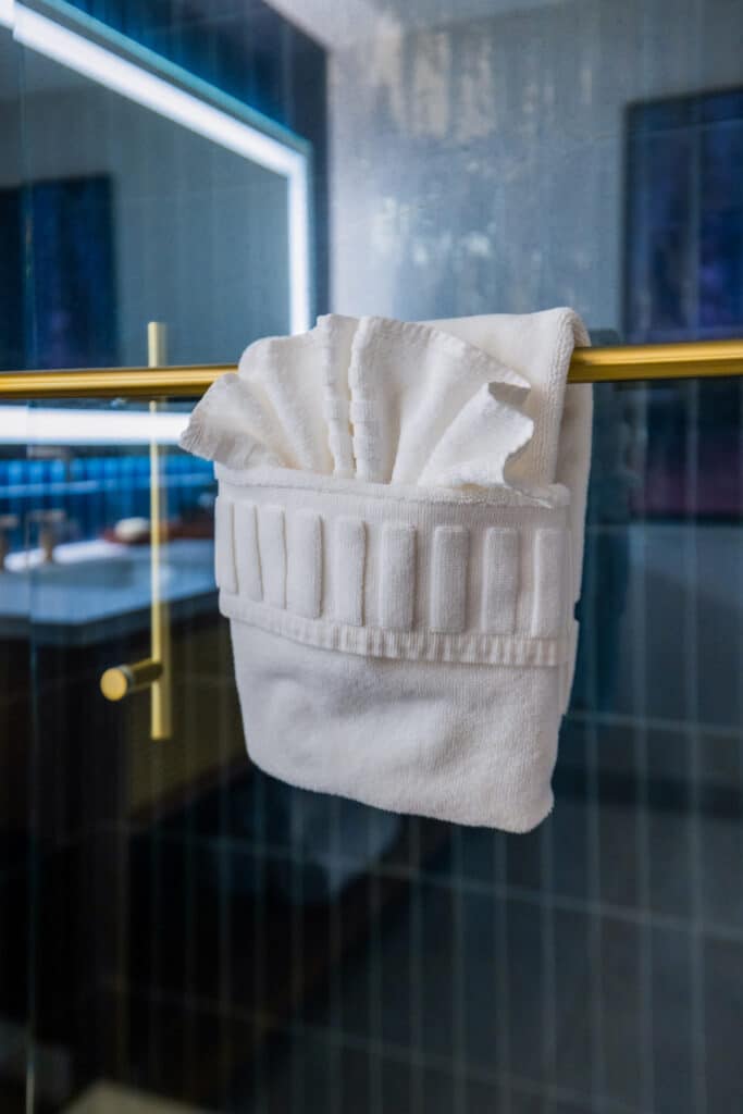 Folded white bath towel draped over a brass shower door handle in a Golden Mesa Hotel bathroom.
