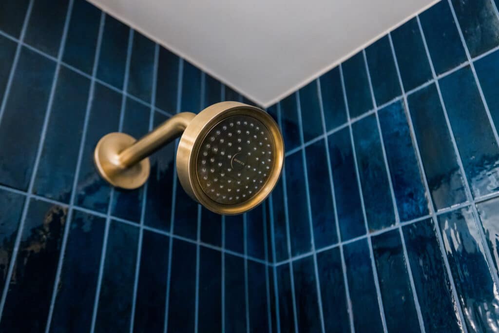 Brass shower head set against deep blue tile in a Golden Mesa hotel bathroom.