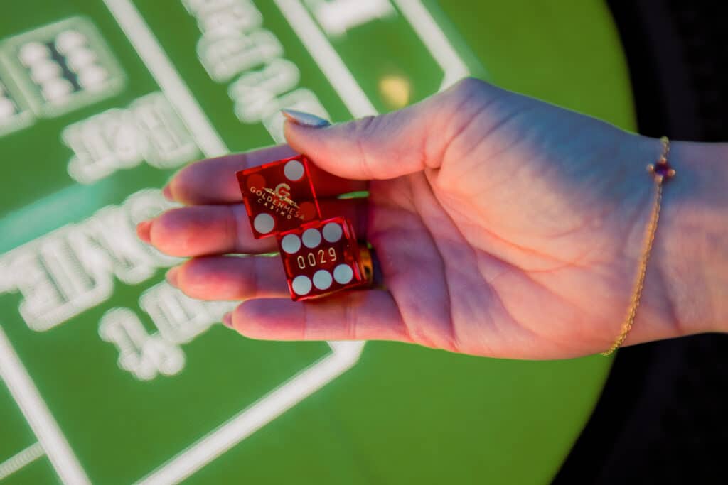 Close-up of a guest holding red Golden Mesa Casino dice over an electronic craps table on the casino floor.
