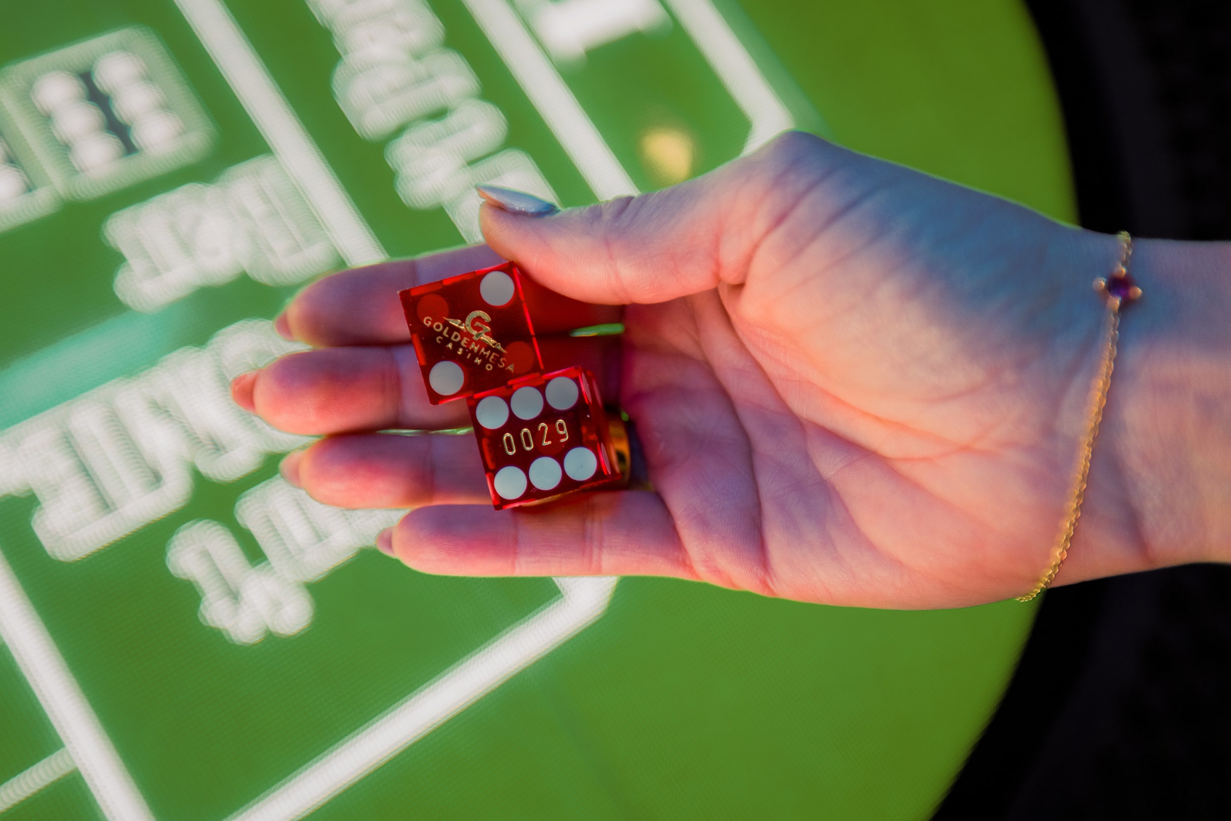 Close-up of a guest holding red Golden Mesa Casino dice over an electronic craps table on the casino floor.