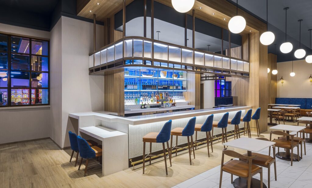 Cimarron Ridge Bar with blue bar seating, warm pendant lights and restaurant tables inside Golden Mesa's Cimarron Ridge Restaurant.