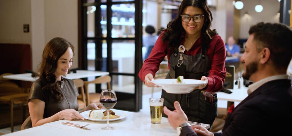 Server bringing a plated meal to guests with wine and beer at Cimarron Ridge Restaurant inside Golden Mesa Casino & Hotel.