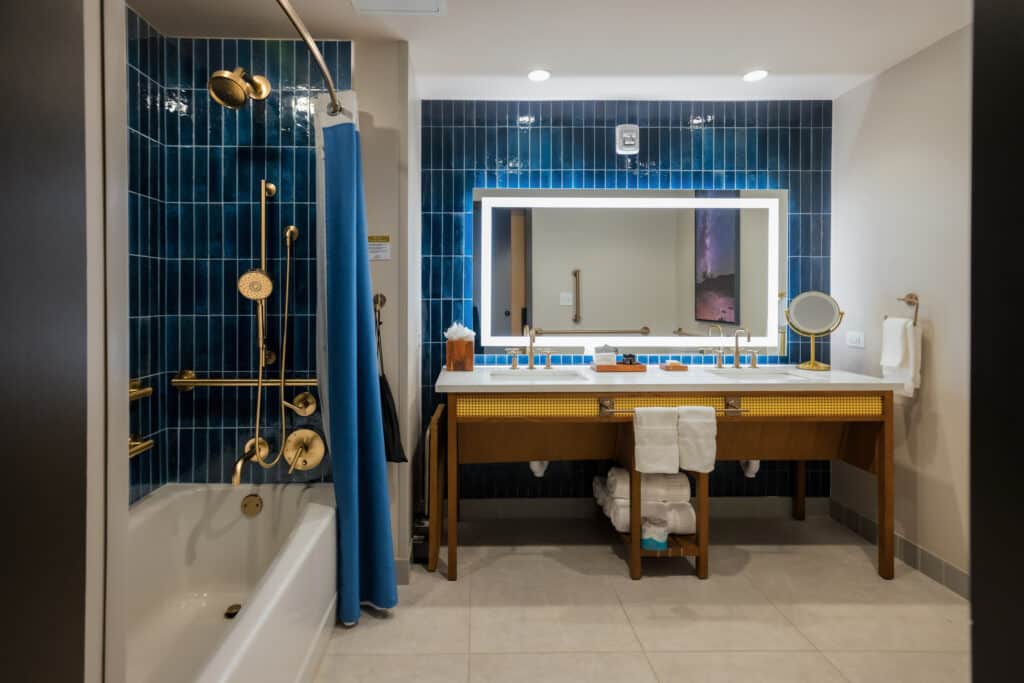ADA accessible tub with grab bars, handheld shower and double-sink vanity in a Golden Mesa Hotel Double Queen bathroom.