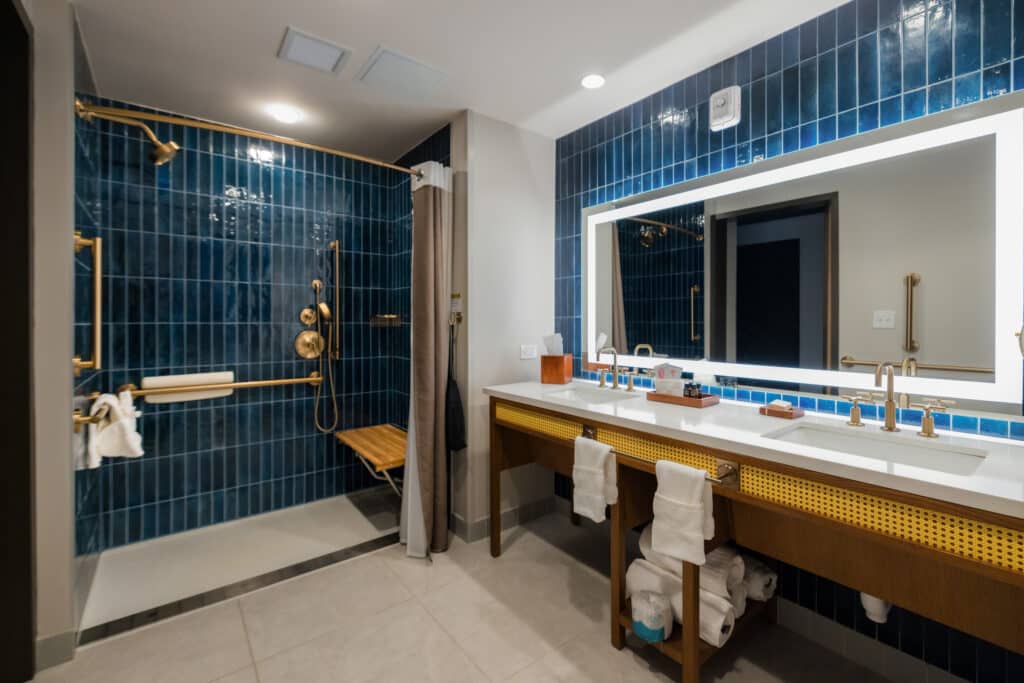 ADA accessible shower with built-in bench, grab bars and double-sink vanity in a Golden Mesa Hotel Double Queen bathroom.