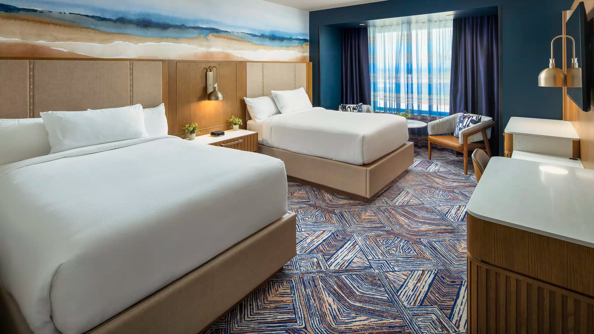 Two queen beds with white bedding, warm bedside lighting and a two-chair seating area in a Golden Mesa Hotel Double Queen room.