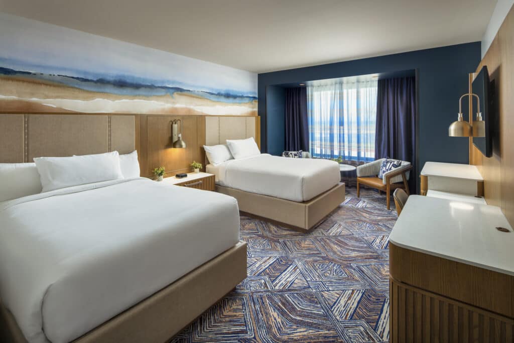 Two queen beds with white bedding, warm bedside lighting and a two-chair seating area in a Golden Mesa Hotel Double Queen room.