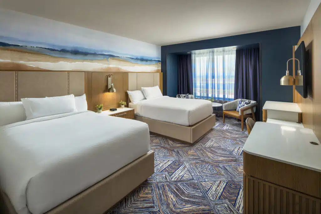 Two queen beds with white bedding, warm bedside lighting and a two-chair seating area in a Golden Mesa Hotel Double Queen room.