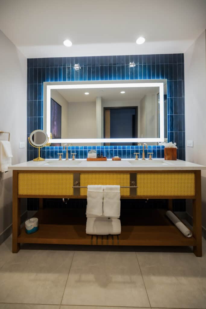 Double Queen bathroom with double-sink vanity, illuminated mirror, soft towels and blue tile at Golden Mesa Hotel.