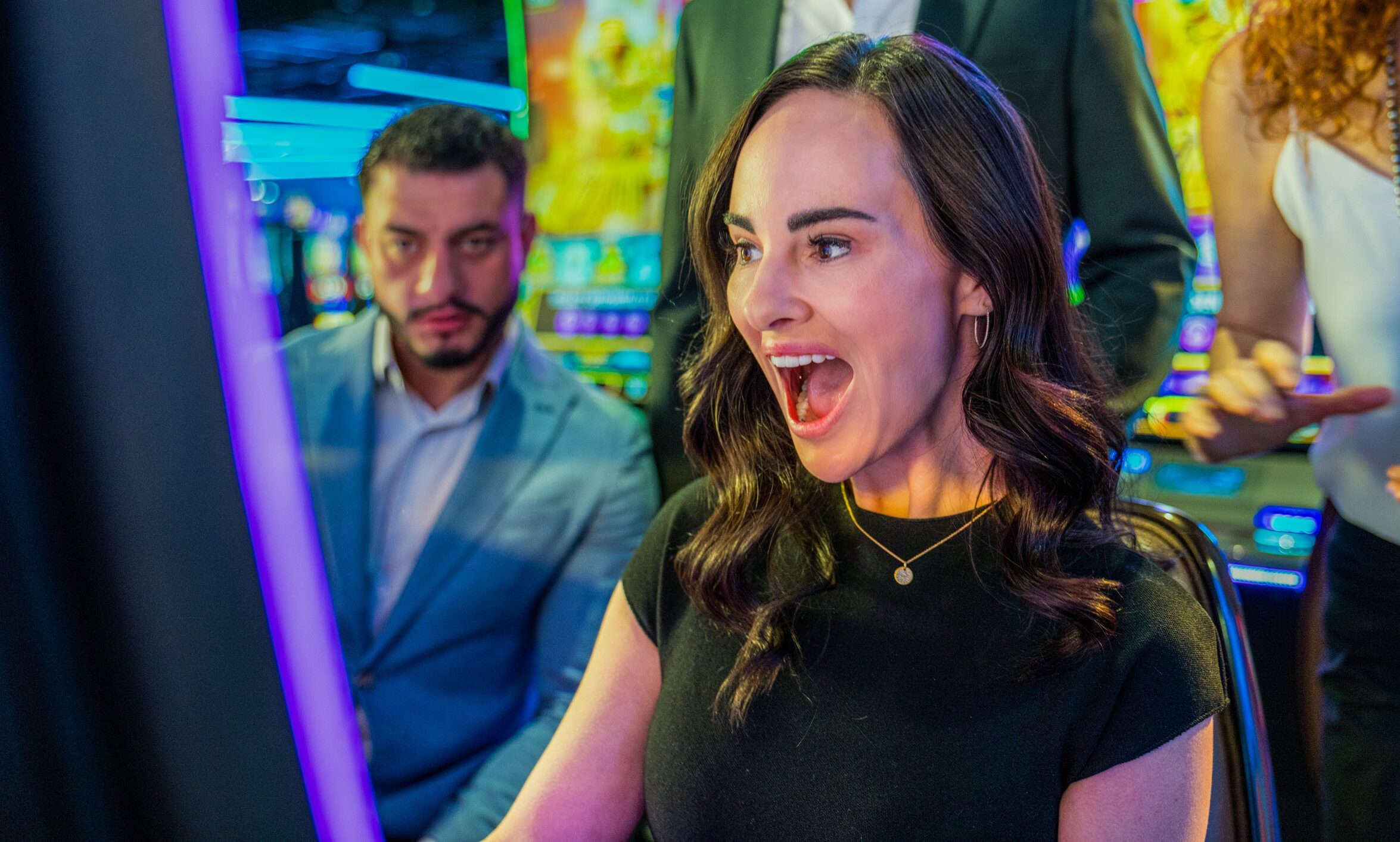 Excited guests reacting while playing a slot machine with other guests and colorful games on the Golden Mesa Casino floor.