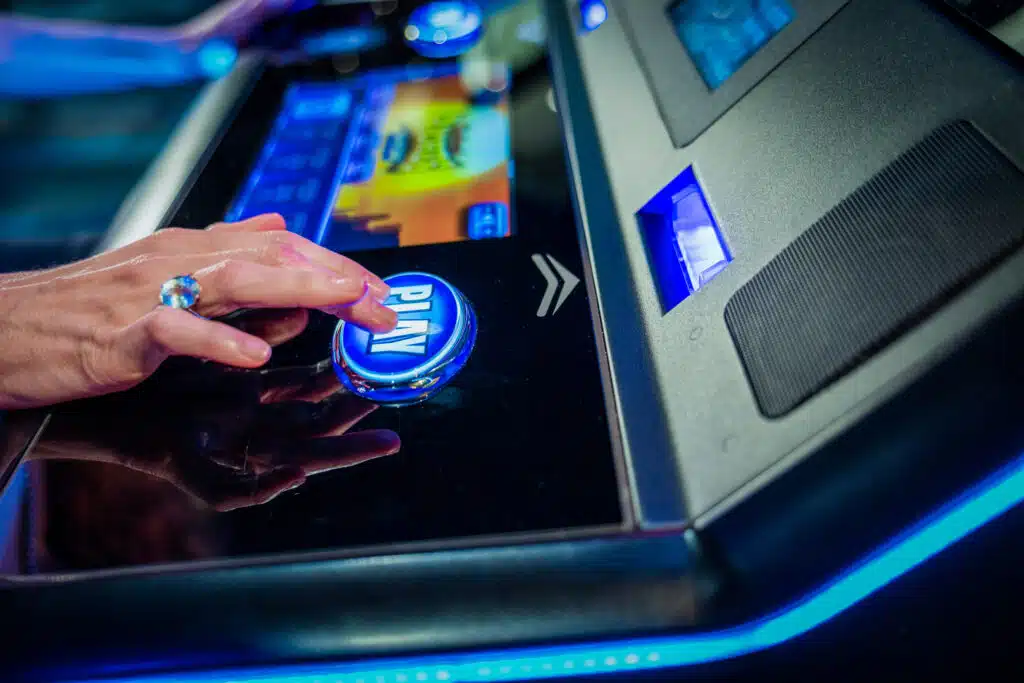 Close-up of a hand pressing the glowing play button on an electronic game at Golden Mesa Casino & Hotel.