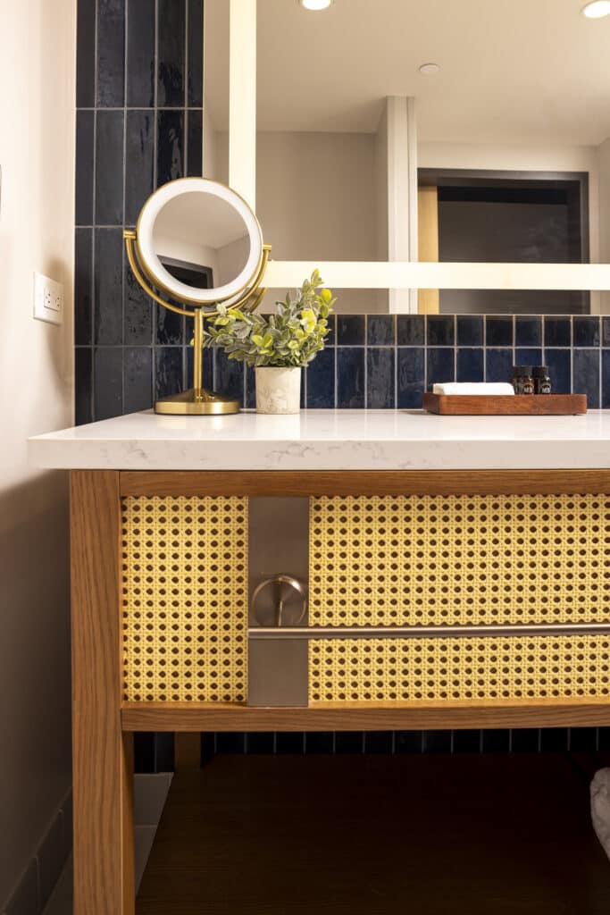 Bathroom vanity with marble countertop, gold mirror, blue tile and woven cabinet detail in a Golden Mesa Hotel room.