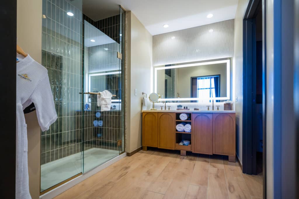 Junior King Suite bathroom with glass shower, white robe, illuminated mirror and spacious vanity at Golden Mesa Hotel.