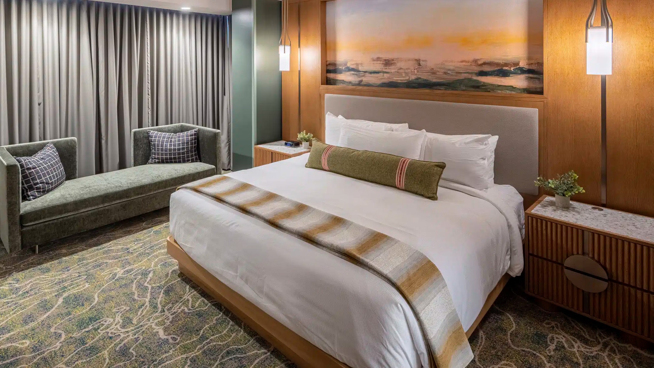 King bed with white bedding, striped throw blanket, warm bedside lighting and elegant couch in a Golden Mesa Hotel Junior King Suite.