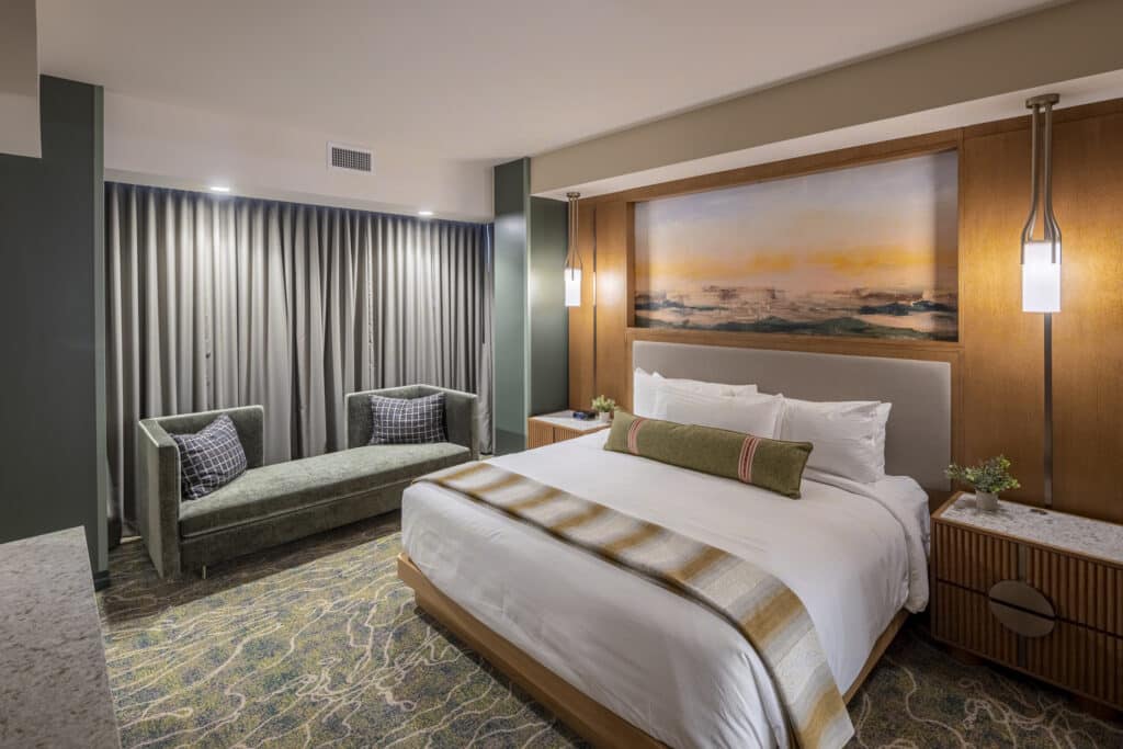King bed with white bedding, striped throw blanket, warm bedside lighting and elegant couch in a Golden Mesa Hotel Junior King Suite.