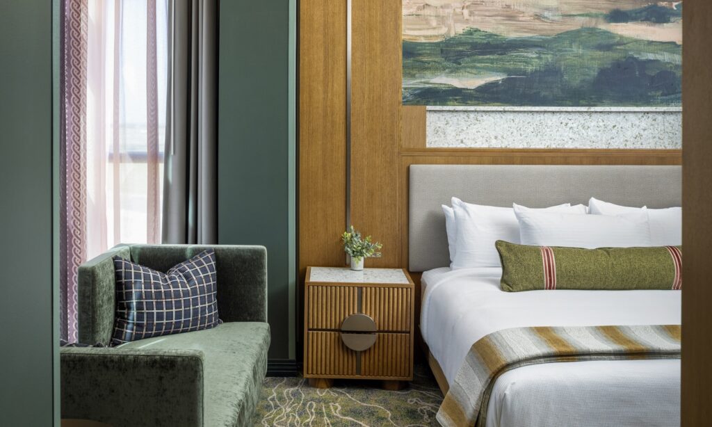 Junior King Suite bedroom viewed from the living area, with green couch, white bedding and wood details at Golden Mesa Hotel.