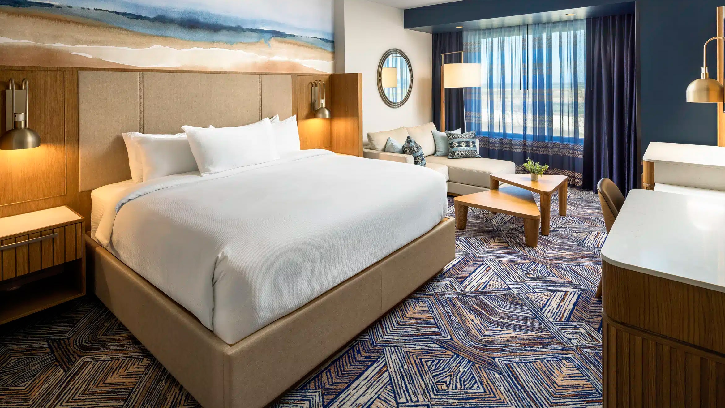 King bed with pristine white bedding and deluxe lounge area with couch and coffee table in a Golden Mesa Hotel King Deluxe room.