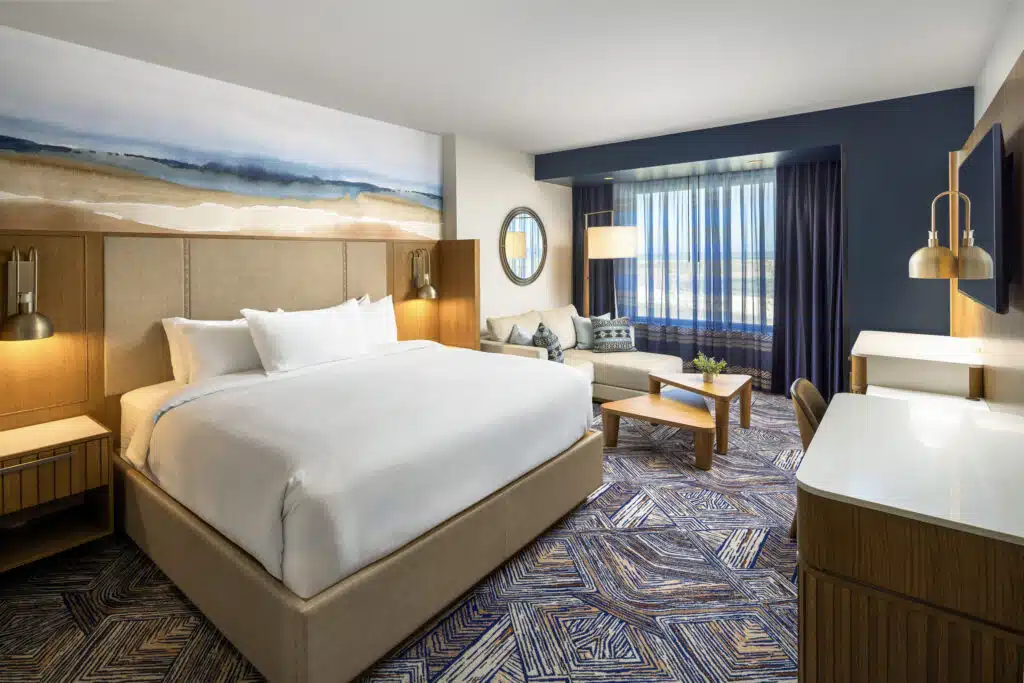 King bed with pristine white bedding and deluxe lounge area with couch and coffee table in a Golden Mesa Hotel King Deluxe room.