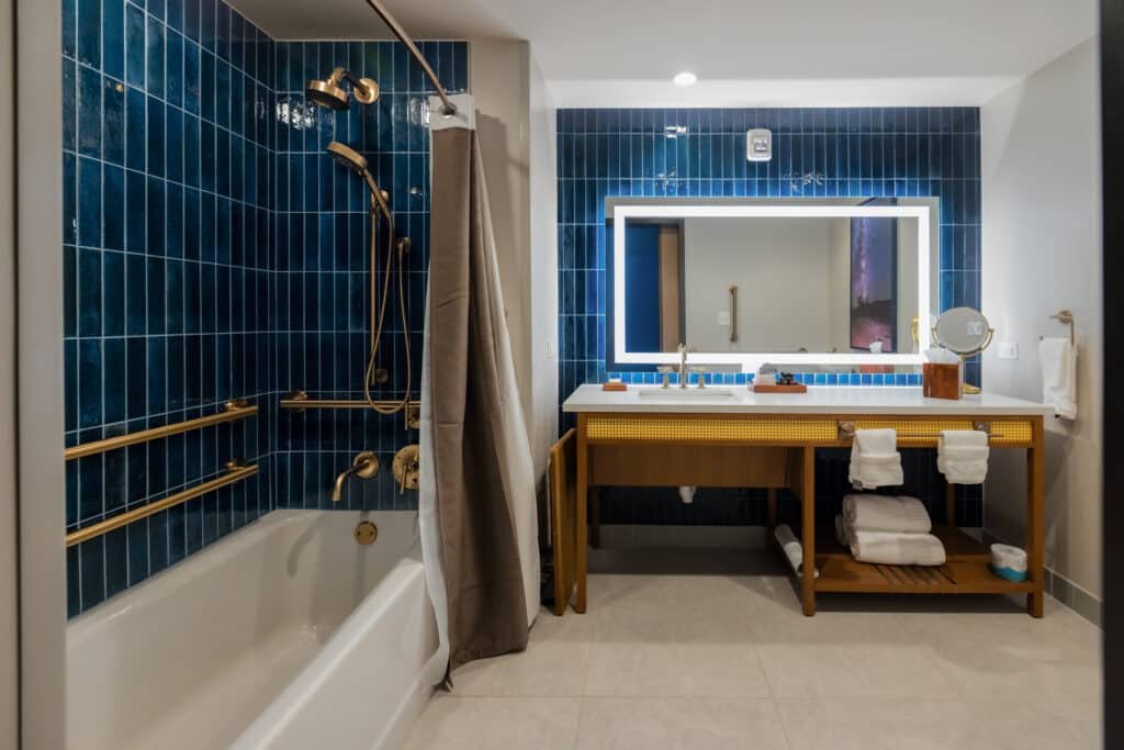 ADA accessible tub with grab bars, handheld shower, blue tile and wide vanity in a Golden Mesa Hotel Standard King bathroom.