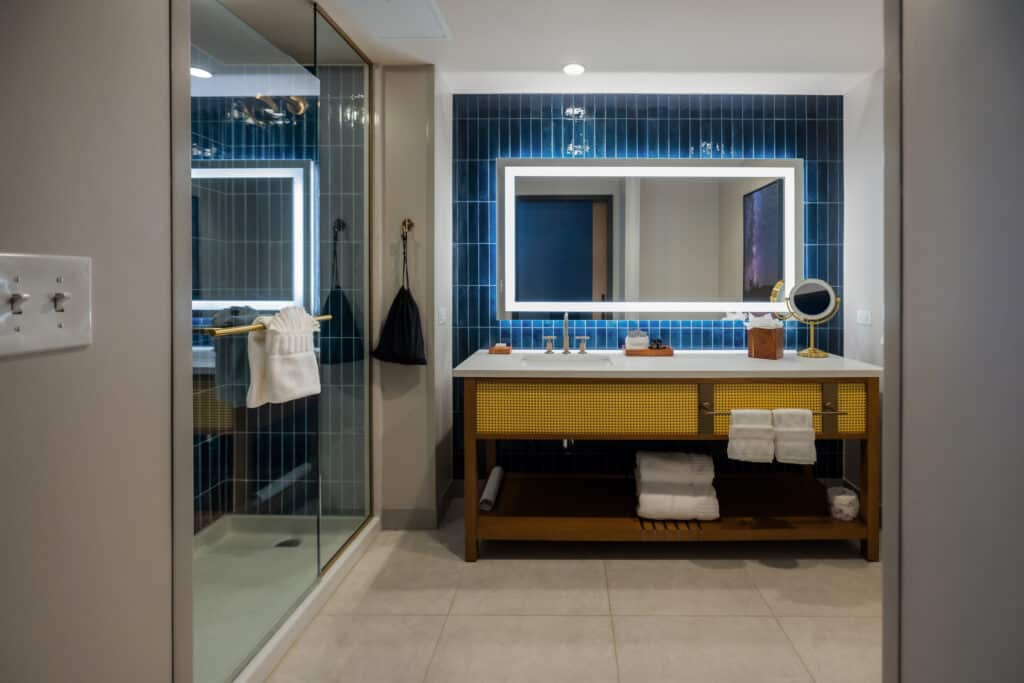 Standard King bathroom with glass shower, deep blue tile, illuminated mirror and wide vanity at Golden Mesa Hotel.