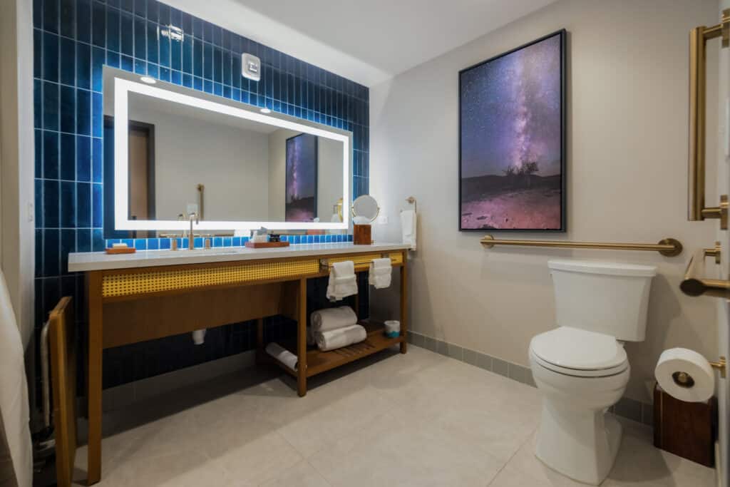 Standard King bathroom with illuminated mirror, blue tile, wide vanity and accessible toilet area at Golden Mesa Hotel.