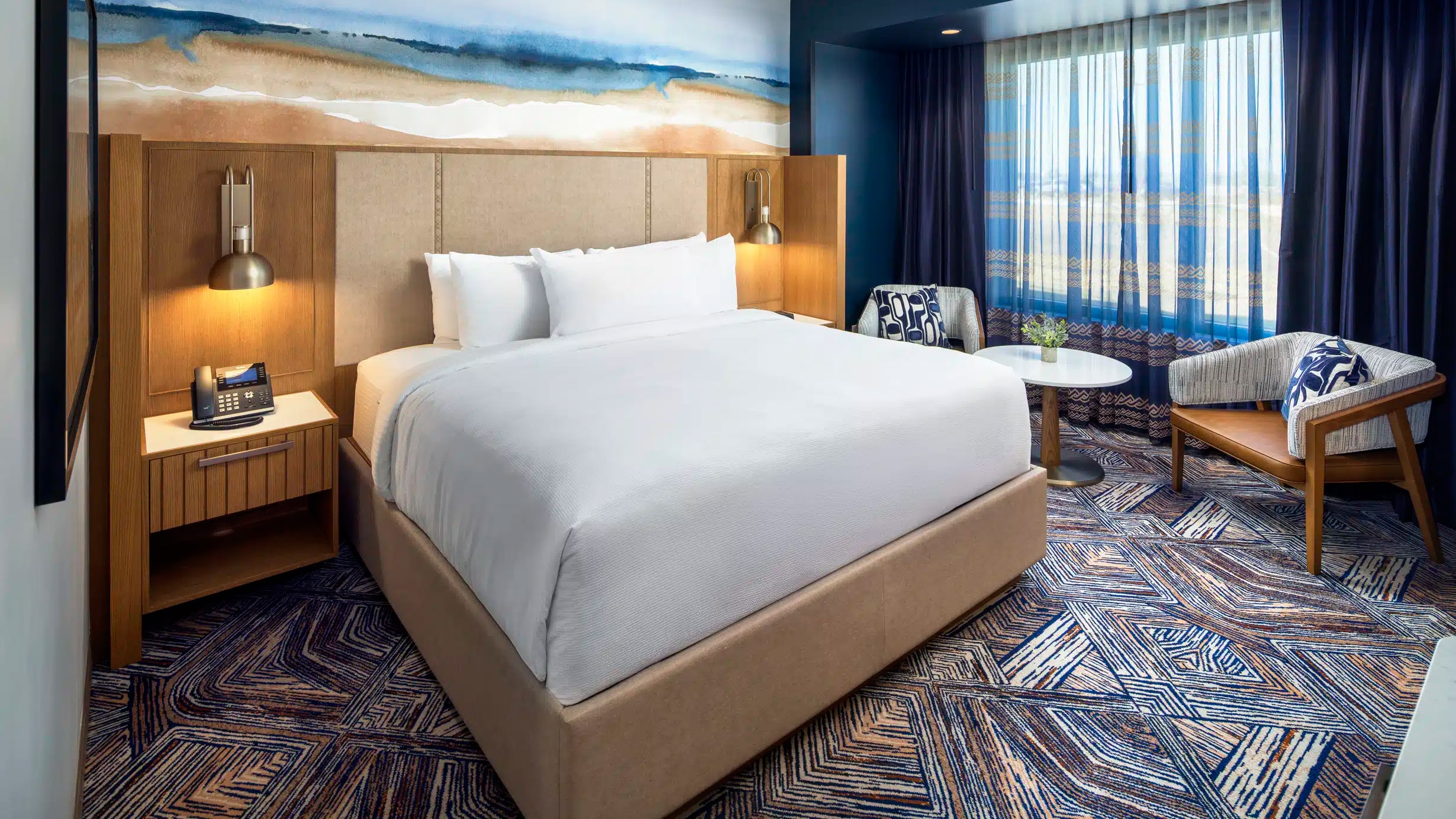King bed with pristine white bedding, soft bedside lighting, and a two-chair seating area in a Golden Mesa Hotel Standard King room.