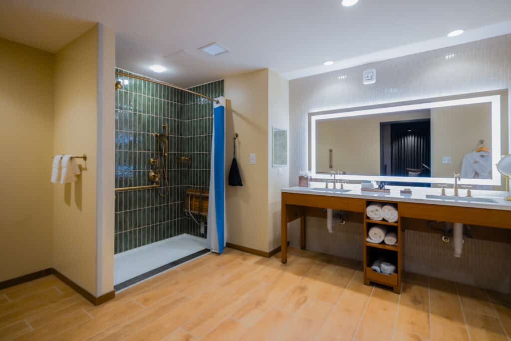 ADA accessible shower with green tile, grab bars, shower seat and wide vanity in a Golden Mesa Hotel King Suite bathroom.