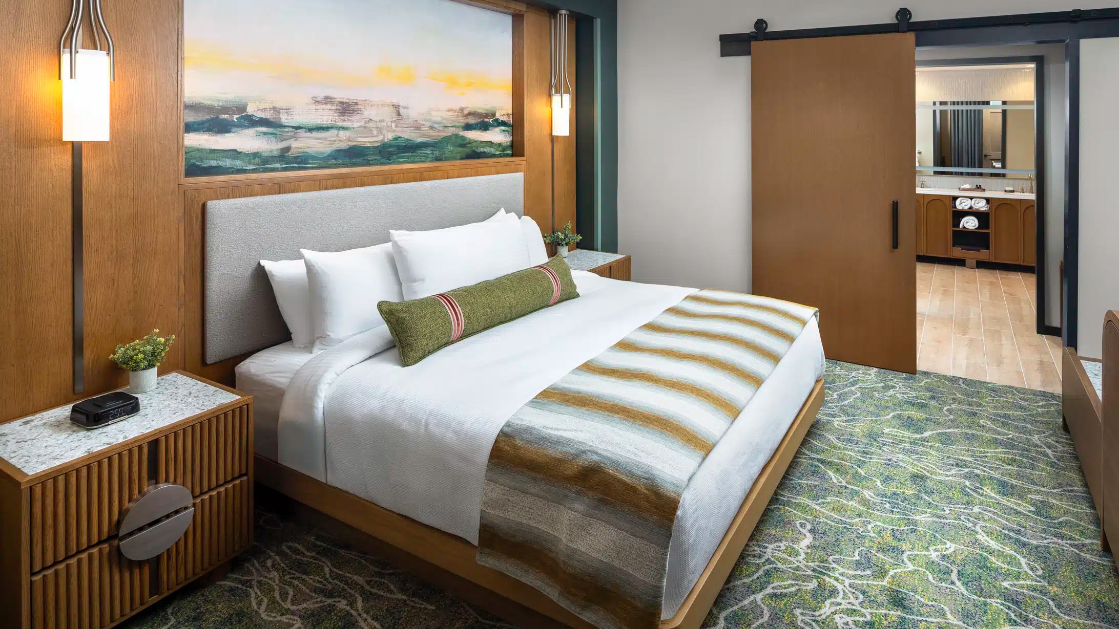 King bed in a Golden Mesa Hotel King Suite with white bedding, warm wood walls and a bathroom beyond.