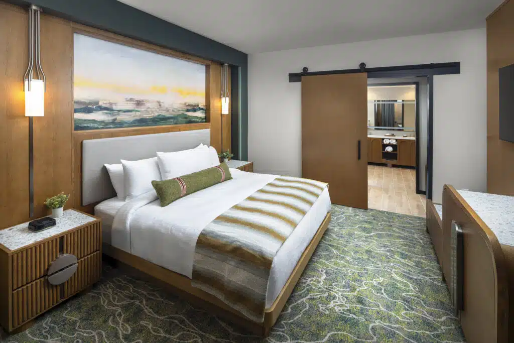 King bed in a Golden Mesa Hotel King Suite with white bedding, warm wood walls and a bathroom beyond.