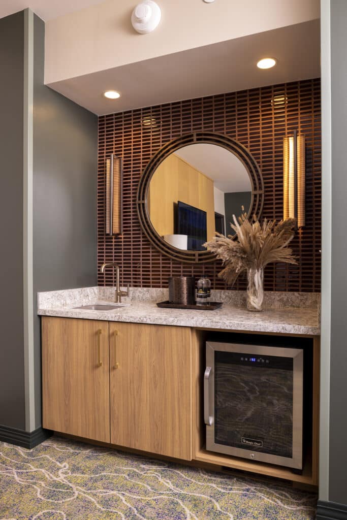 King Suite wet bar with mini fridge, sink, round mirror, marble countertop and warm lighting at Golden Mesa Hotel.