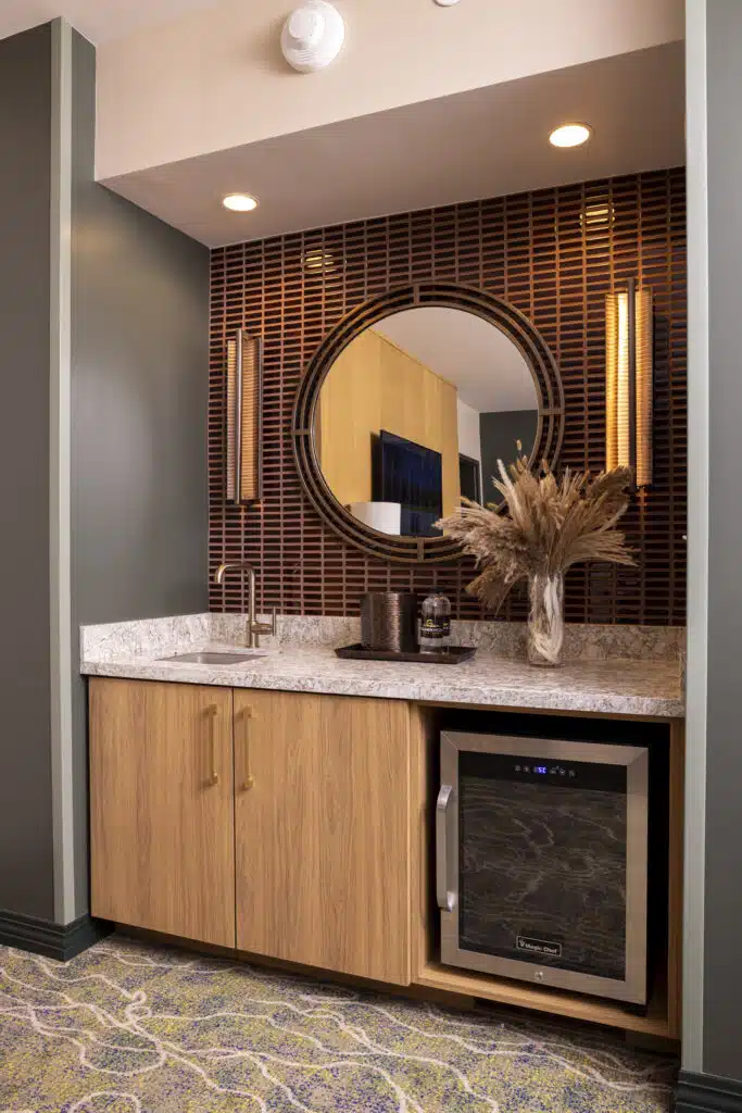 King Suite wet bar with mini fridge, sink, round mirror, marble countertop and warm lighting at Golden Mesa Hotel.