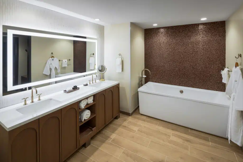 King Suite bathroom with full bathtub, double vanity, illuminated mirror and white robes at Golden Mesa Hotel.