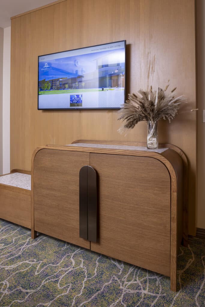 Wall-mounted TV, polished wood storage cabinet and decorative vase in a Golden Mesa Hotel King Suite.