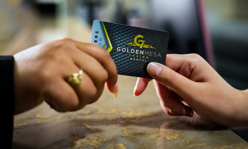Close-up of the hands of a Golden Mesa Casino employee handing a Players Club card to a player at the Players Club desk.