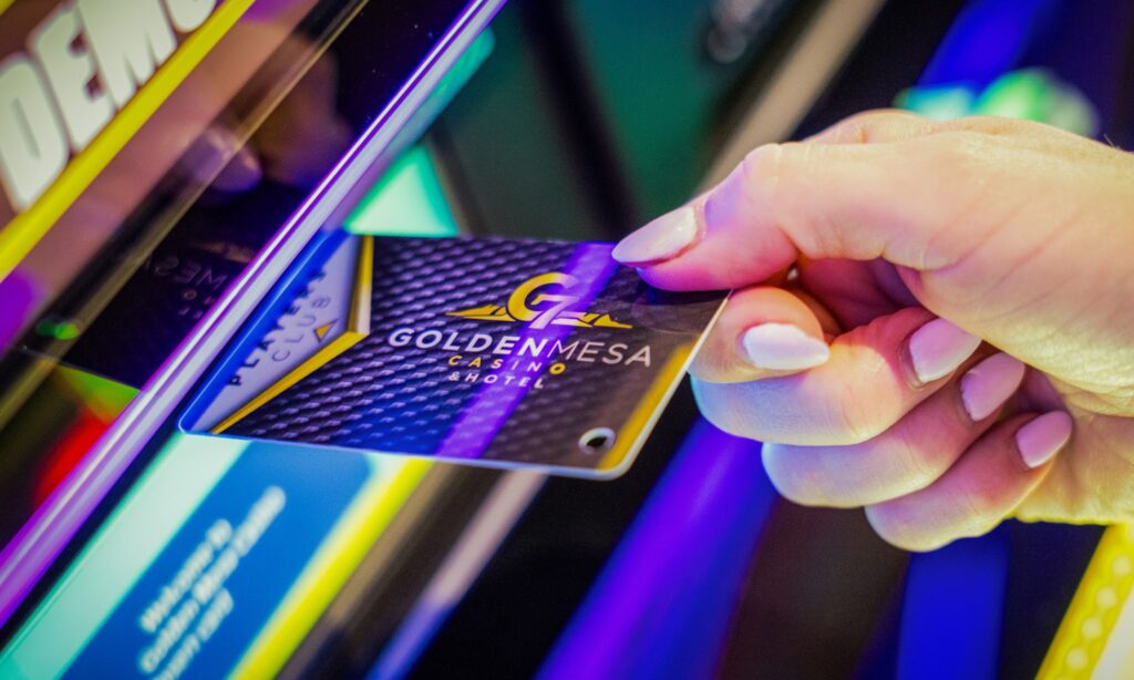Close-up of a guest inserting a Golden Mesa Players Club card into an electronic game, with colorful casino lights glowing.