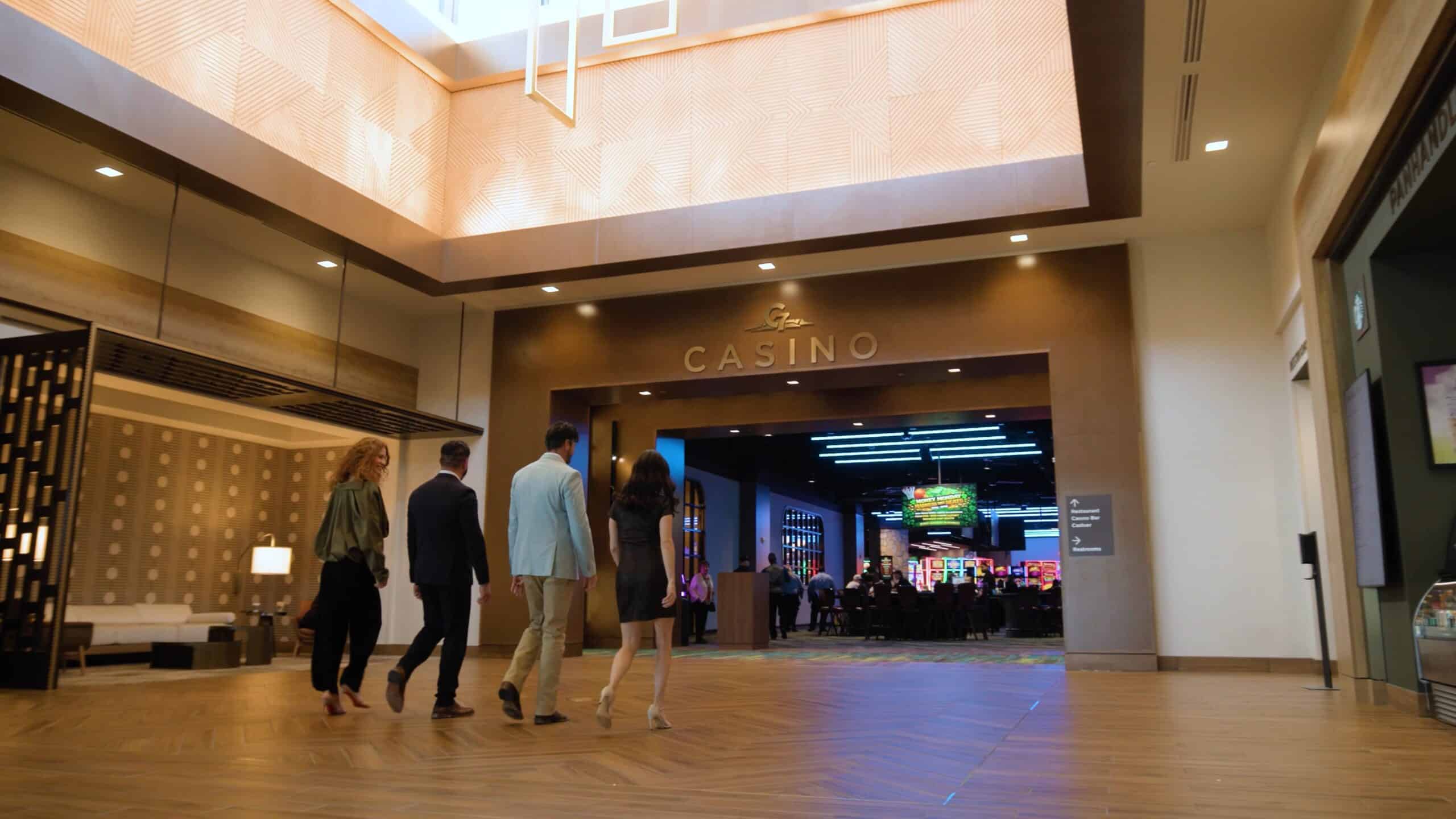 Guests walking from the Golden Mesa Hotel lobby toward the casino entrance, with warm lighting and gaming floor beyond.
