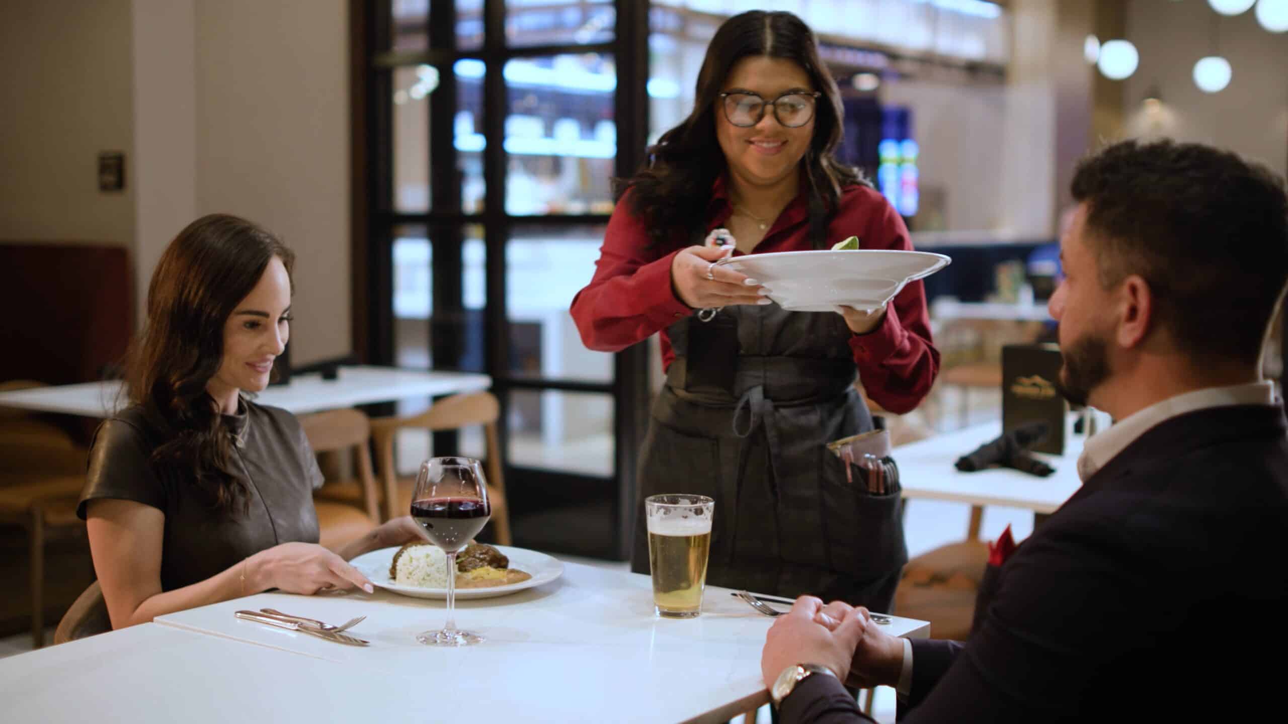 Server bringing a plated meal to guests with wine and beer at Cimarron Ridge Restaurant inside Golden Mesa Casino & Hotel.