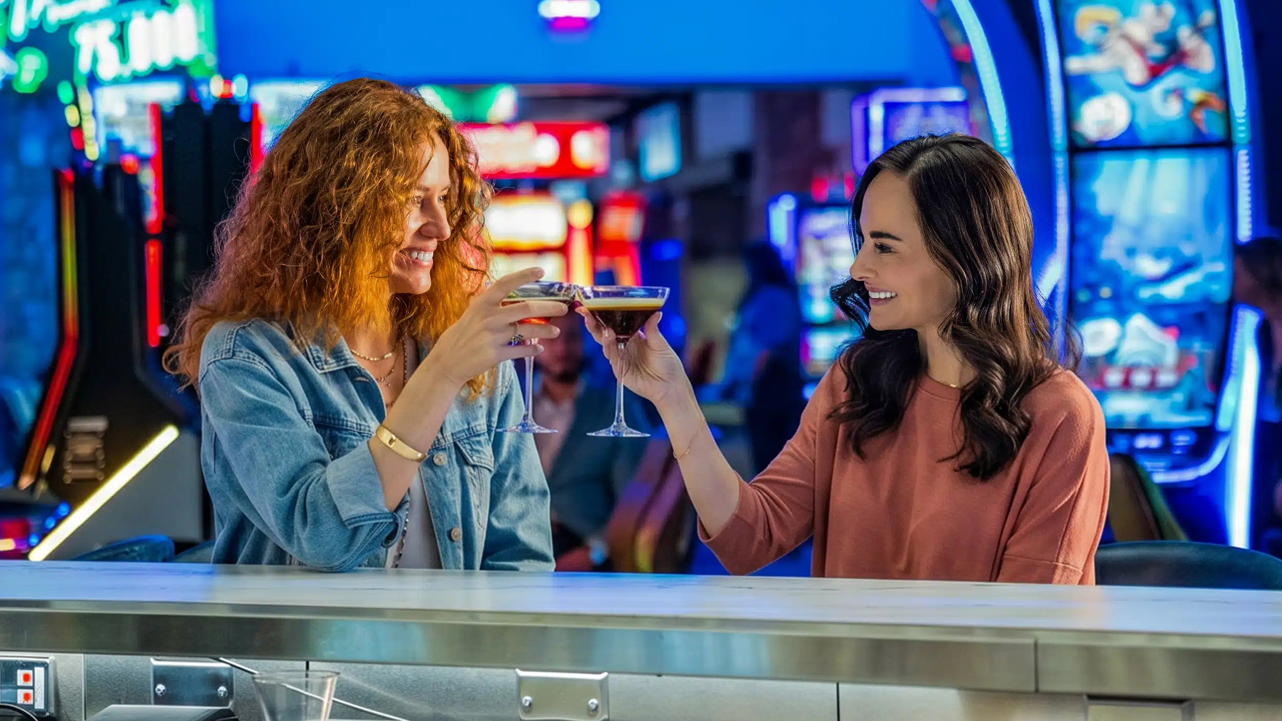 Two guests clink espresso martinis at Cimarron Ridge Bar inside Golden Mesa Casino, with colorful slot machines behind them.