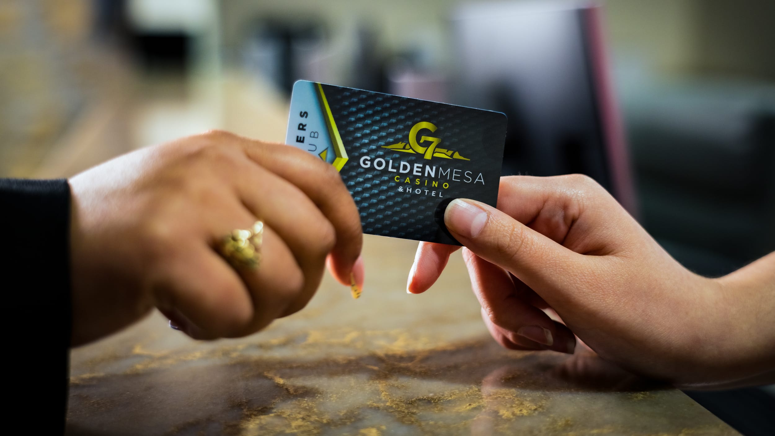 Close-up of the hands of a Golden Mesa Casino employee handing a Players Club card to a player at the Players Club desk.