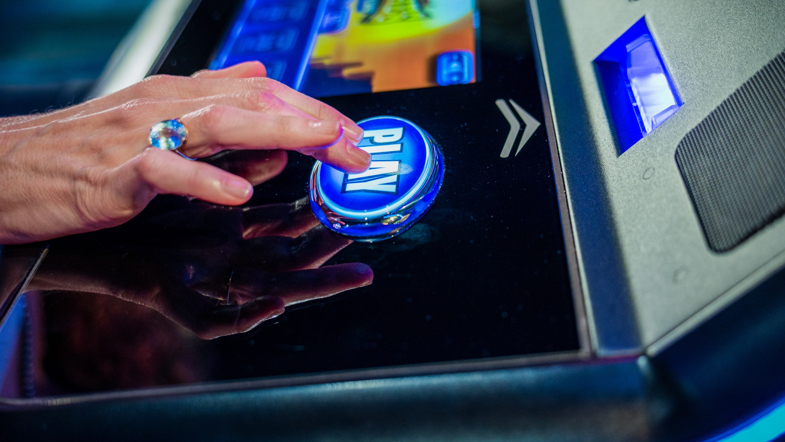 Close-up of a hand pressing the glowing play button on an electronic game at Golden Mesa Casino & Hotel.